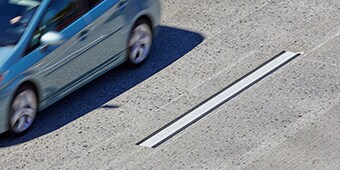 A blue car speeds past a high-contrast road marking that is easily visible on the pavement.
