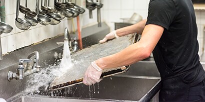 Um lavador de louças de restaurante limpando uma assadeira em uma pia comercial.
