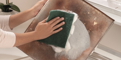 Uma pessoa lavando uma chapa de hamburguer com uma esponja verde.