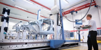 Pessoa trabalhando no display de uma máquina no interior de uma fábrica.
