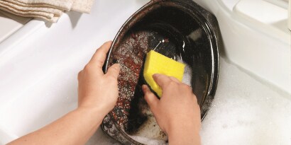 Uma pessoa lavando uma vasilha suja com uma esponja verde e amarela.