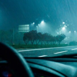 Image of view from in a car looking straight ahead to the road, it's night and it's raining, and there is reflective tape on the road.