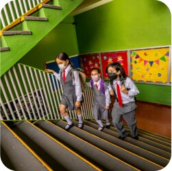 Three girls in their school uniforms climbing the stairs en route to class.
