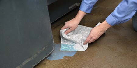 Pessoa usando o kit de derramamento 3M para absorver um derramamento de líquido no chão.
