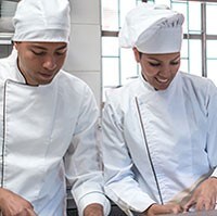 Dois chefes de cozinha em roupas brancas conversam em uma cozinha comercial.