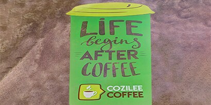 A green floor graphic in the shape of a cup reads, “Life begins after coffee.”
