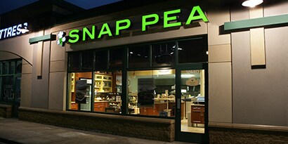 Green illuminated letters reading “Snap Pea” advertise a restaurant.
