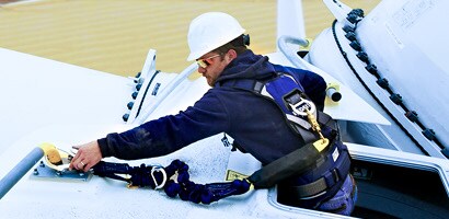 Worker reaching out of access port in wind turbine and fastening lanyard to anchor point
