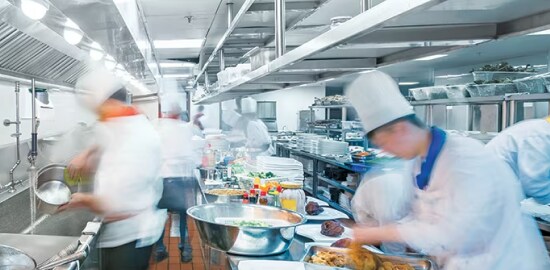 Uma cozinha comercial com vários chefes de cozinha preparando comida.
