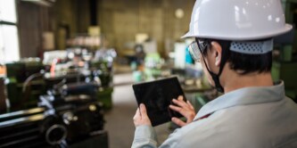 Pessoa com um capacete branco segurando um tablet e tocando em sua tela. 
