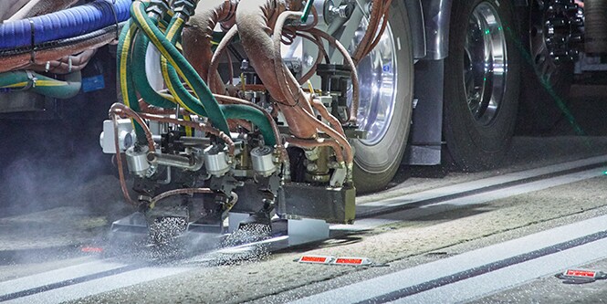 A truck applies liquid pavement markings with double-drop optics system on the roadway.
