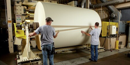 Image of workers taping down the tail of a large paper roll
