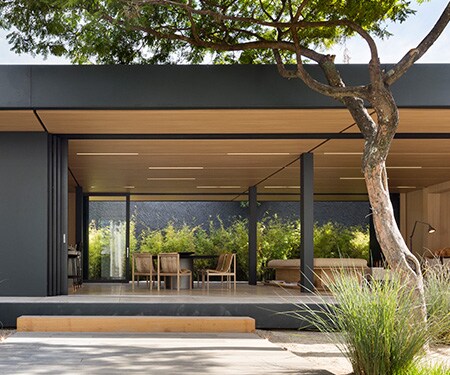 Exterior de uma casa moderna com acabamentos em preto fosco e madeira clara.
