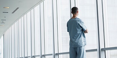 Homem olhando pela janela limpa de uma instalação de saúde.
