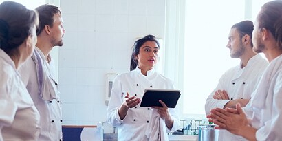 Cinco funcionários discutindo, um deles segurando um tablet.
