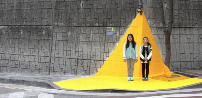 Two young girls in South Korea waiting to cross the street standing on a 'yellow carpet.'
