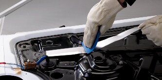A worker applies a damping foil tape to a metal frame to help damp vibration and noise
