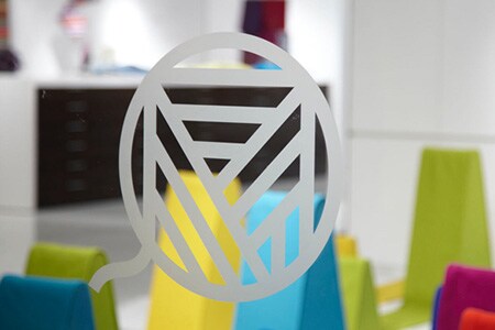 Janela de vidro transparente com logotipo em arte com linhas estilo vidro jateado com formas coloridas no fundo.
