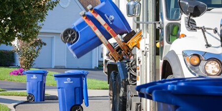 Uma lixeira de reciclagem azul sendo levantada para um caminhão de reciclagem.
