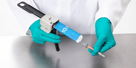 A gloved worker attaches a mixing nozzle to a 10-to-1 Duo Pak adhesive held in an EPX applicator
