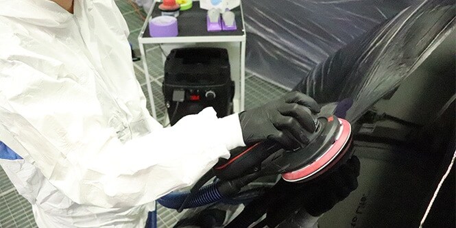 Trabalhador em uma oficina utilizando uma lixadeira do Sistema de Lixamento Limpo da 3M na superfície de um veículo.

