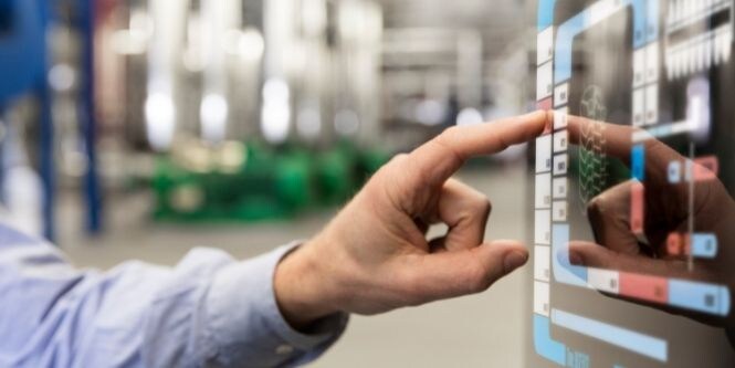 Imagem de um operário de fábrica utilizando uma tela touchscreen na linha de montagem.
