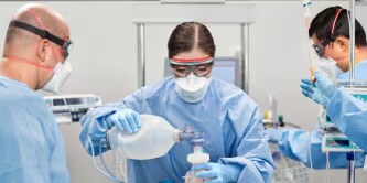 Três profissionais de saúde estão prestando cuidados a um paciente utilizando equipamento de proteção individual (EPI) da 3M.
