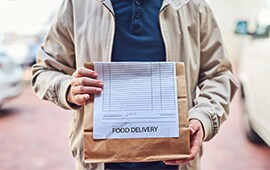 delivery service driver carrying a brown bag of take-out with a customer's order receipt stapled to the bag