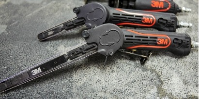 Pessoa cobrindo um carro preto com um filme plástico transparente de proteção em ambiente de oficina com parede de tijolos.
