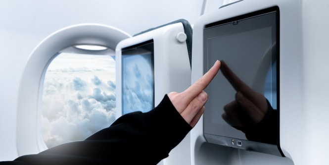 Pessoa em um avião tocando na tela de TV no encosto do assento à sua frente.
