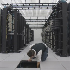 An IT specialist reaches into the floor of a data center, where fans are stored