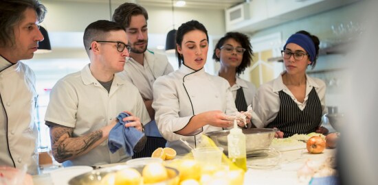 Uma chef principal treinando novos funcionários em uma cozinha comercial.
