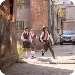Three kids walking home from school in an urban neighborhood setting.
