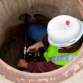 Electrician in a manhole repairing wire with electrical tape.