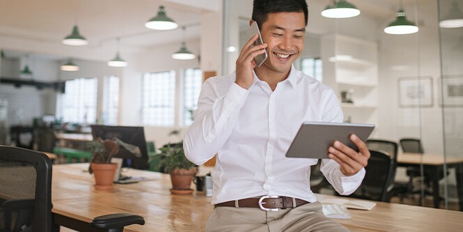 Imagem de homem de negócios sorridente falando ao telefone e olhando para um tablet.

