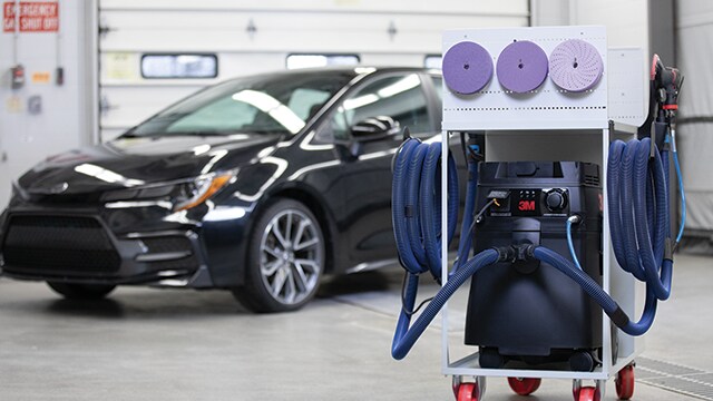 Carrinho de lixamento e extração de poeiras 3M em uma oficina com um veículo ao fundo
