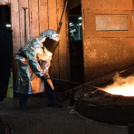 Trabalhador com equipamento de proteção individual trabalhando em um processo de fundição.