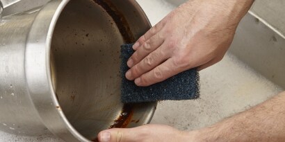 Uma pessoa lavando uma assadeira de alumínio com uma esponja verde.