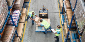 Vista aérea de trabalhadores transferindo caixas de um palete para uma prateleira.
